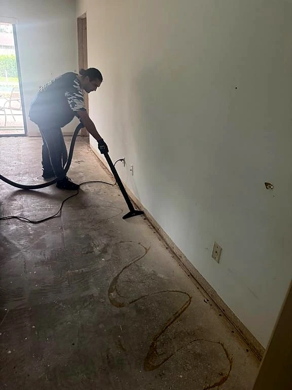 A technician cleans the exposed floor along the base of a wall.