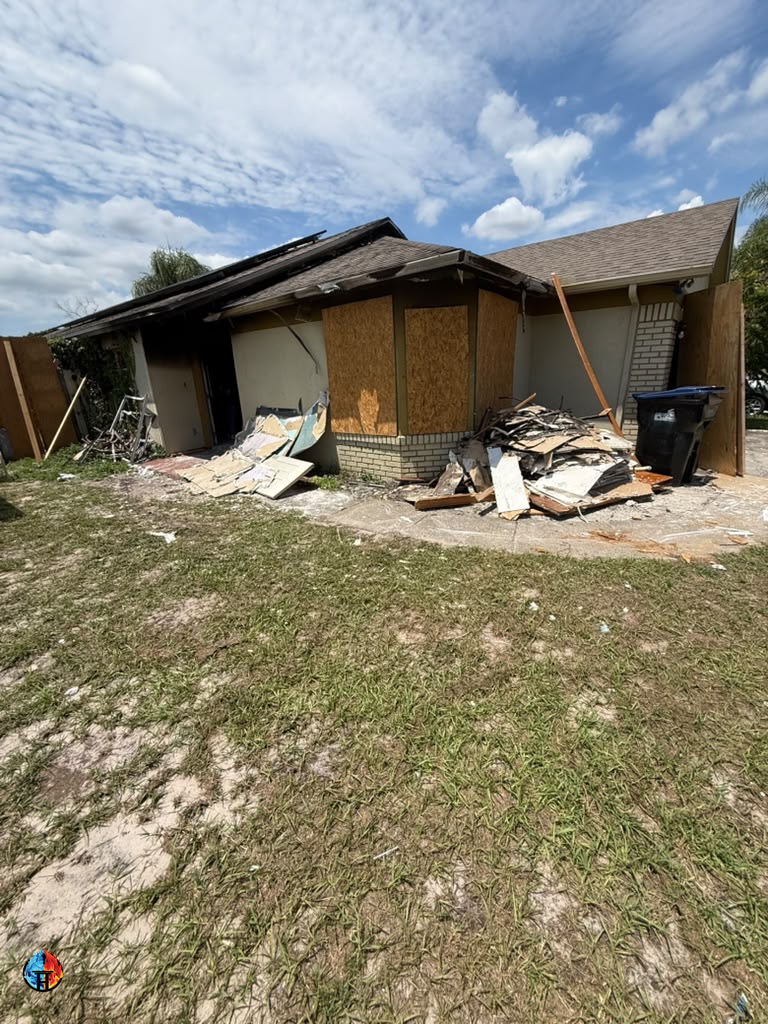 Boarded house with damaged materials piled beside the driveway