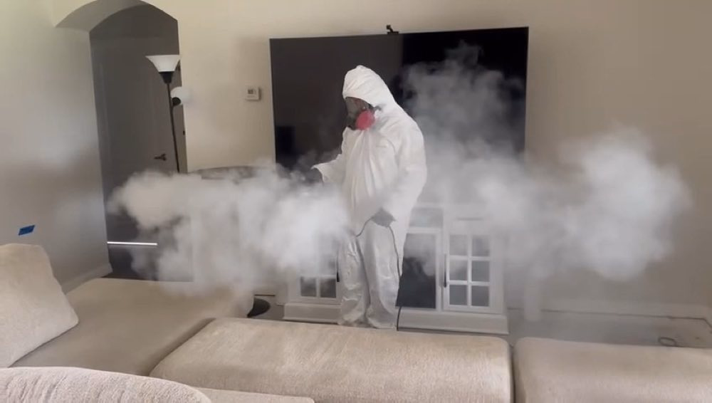 Worker using misting equipment inside a furnished room